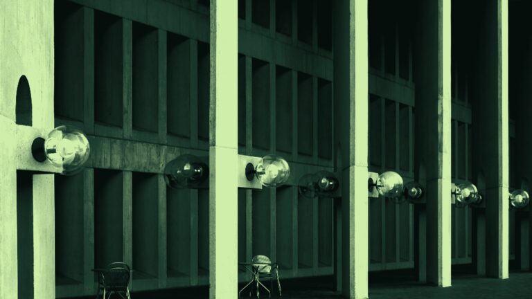 Rij betonnen pijlers met bollampen langs de gevel van een modern gebouw